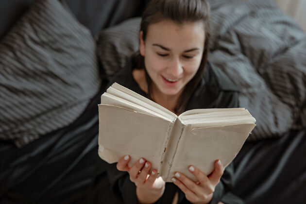 女孩穿着睡衣的迷人的年轻女子正在床上看书放松年轻室内舒适