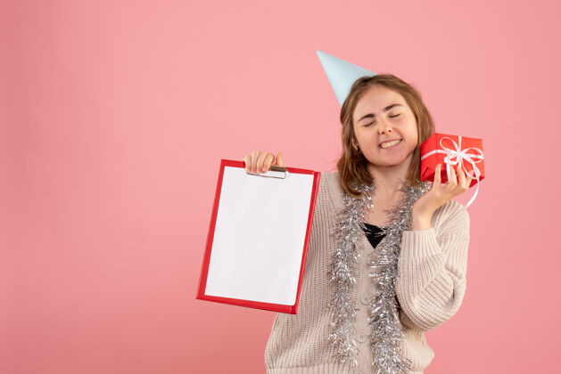 粉红色年轻的女性拿着小圣诞礼物和粉红色的纸条举行便条礼物