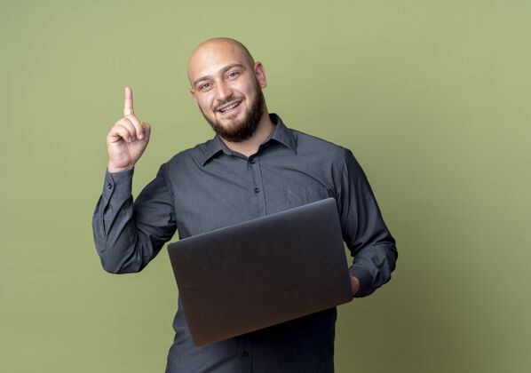 提高令人印象深刻的年轻秃顶呼叫中心男子手持笔记本电脑 举起手指孤立在橄榄绿与复制空间复制中心橄榄