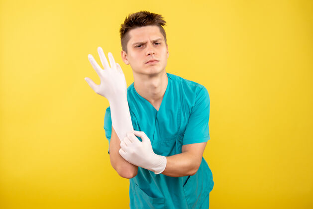 年轻男性医生正面图年轻的男医生穿着医疗服 戴着黄色背景的手套健康人成功