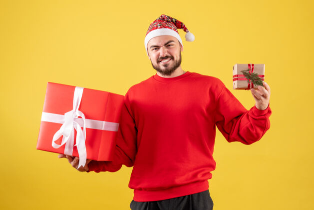 人黄色背景下手持圣诞礼物的年轻男性正面图微笑年轻男性礼物