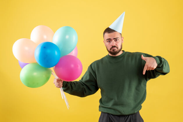 背景正面图黄色背景上有彩色气球的年轻男性快乐庆祝气球