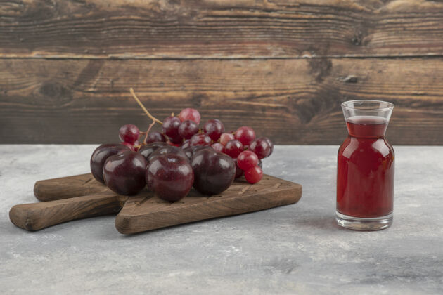 李子用新鲜的红李子和葡萄做成的木板 大理石表面有一杯果汁成熟果汁女