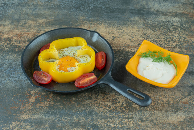 一餐一个深色的平底锅 大理石背景上有煎蛋 西红柿和酸奶油好吃的蛋黄西红柿