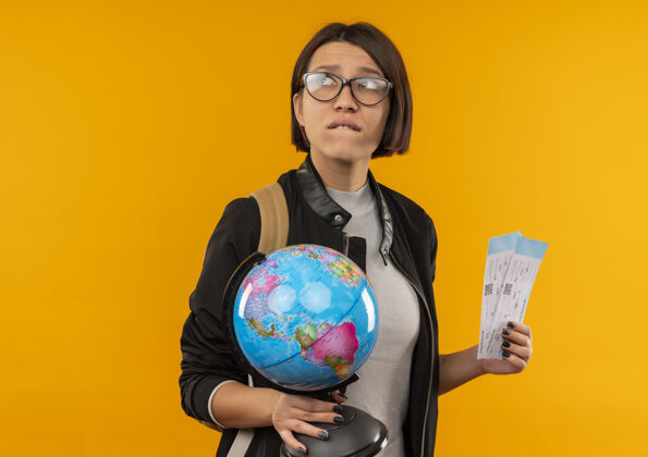 复制焦急的年轻女学生戴着眼镜 背着包拿着地球仪和票 看着一边孤立的橘黄色带着复印空间票眼镜学生
