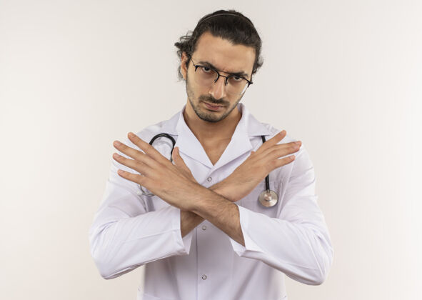 手势严格的年轻男性医生 戴着眼镜 穿着白色长袍 听诊器 在隔离的白色墙壁上显示“不”的手势 并留有复印空间表演年轻严格
