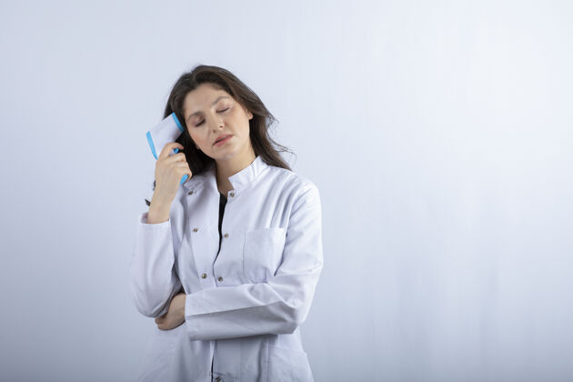 工作女医生拿着温度计站在白墙上女性温度计站立