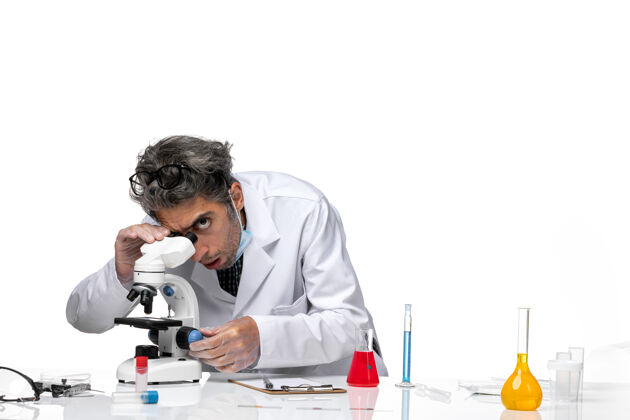 实验室穿着白色医疗服的中年科学家使用显微镜的正视图病毒办公桌前台