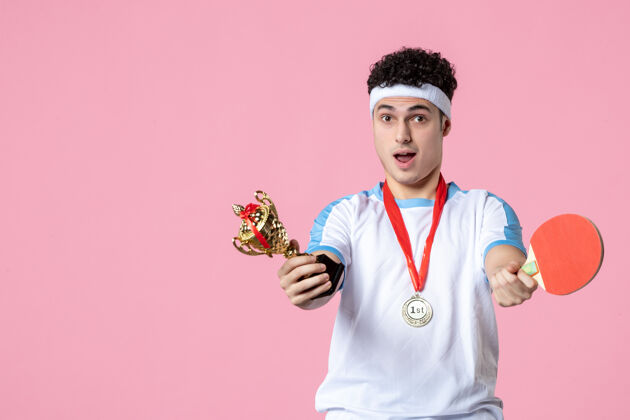 奖牌正面图身穿运动服的年轻男性 粉色墙上有奖牌和金杯粉红色成功体育