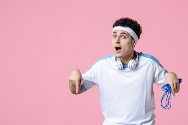 绳子正面图：穿着运动服的年轻男性 粉色墙上挂着跳绳运动指向下年轻男性