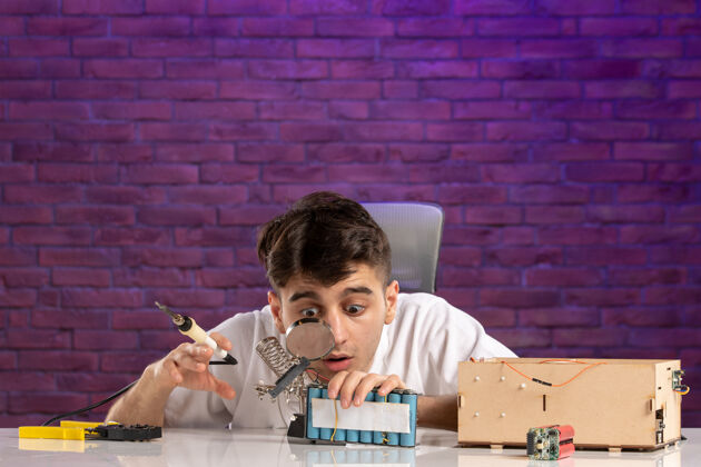 工作前视图：桌子后面的年轻男子正试图把小房子的布局固定在紫色的墙上年轻男性专业建筑商