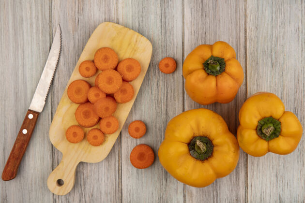 膳食顶视图新鲜的橙色甜椒与切碎的胡萝卜在一个木制的厨房板上用刀在灰色的木墙上胡萝卜铃铛自然