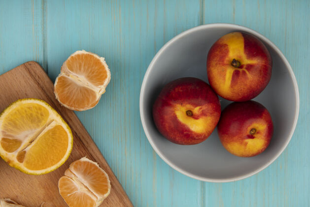 木材新鲜的桃子放在碗上 橘子放在蓝色的木墙上的木制厨房板上顶部观点桃