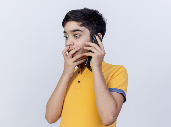 下来惊讶的年轻白人男孩在讲电话 手放在嘴上 看着白色背景上的空白年轻男孩嘴