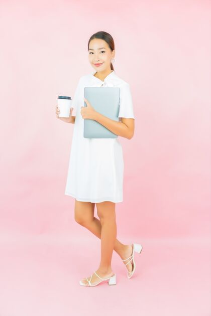 女性肖像美丽的亚洲年轻女子在粉红色的墙上用笔记本电脑年轻人学习公司