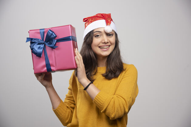 微笑戴着圣诞帽拿着礼盒的年轻女子礼品盒黑发女士