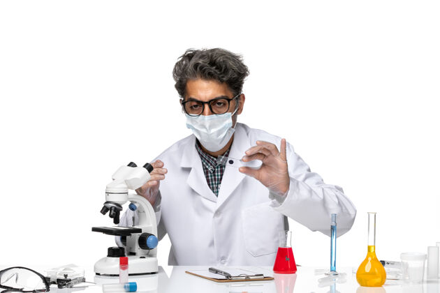实验室前视图中年科学家穿着医疗服通过显微镜检查小样本专业视图外套