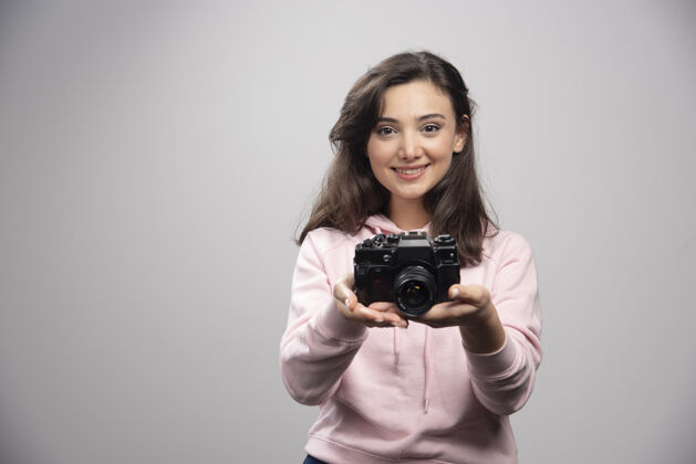 可爱女摄影师带着相机在灰色的墙上微笑人爱好女性