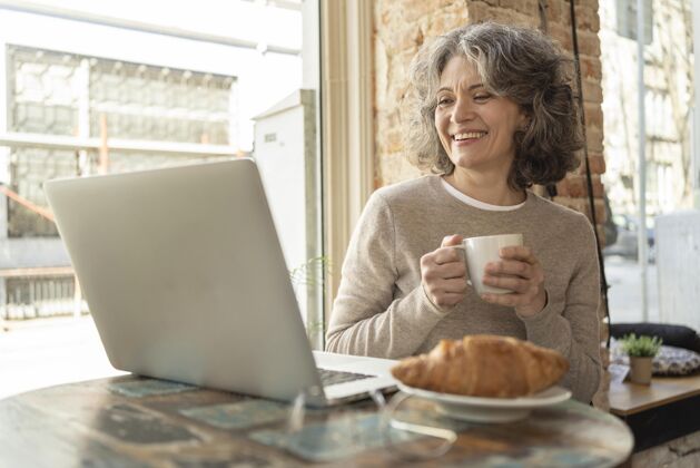 羊角面包一个喝咖啡的女人肖像笔记本电脑现代女人