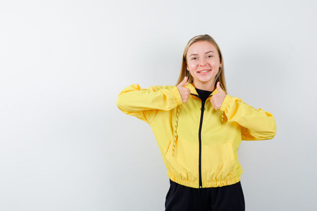 女性穿着黄色夹克 裤子的年轻女士向上竖起大拇指 看上去很快乐 正前方模特美容裤子