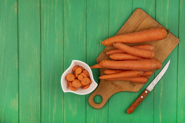 木材新鲜胡萝卜的顶视图在一个木制的厨房板上用刀在一个绿色的木制墙壁上复制空间饮食板顶部