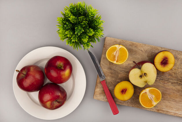 木头在灰色的墙上 用刀将桃子 苹果和橘子等甜味水果隔离在木制的厨房板上 盘子上放着红苹果苹果食物人