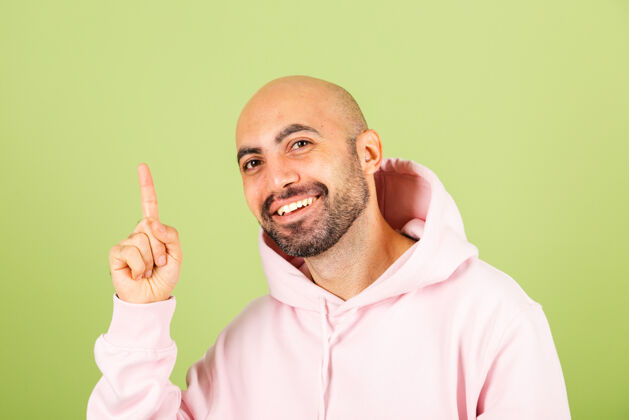 成人年轻秃顶的白种人 穿着粉色连帽衫 面带微笑 手指朝上快乐肖像向上