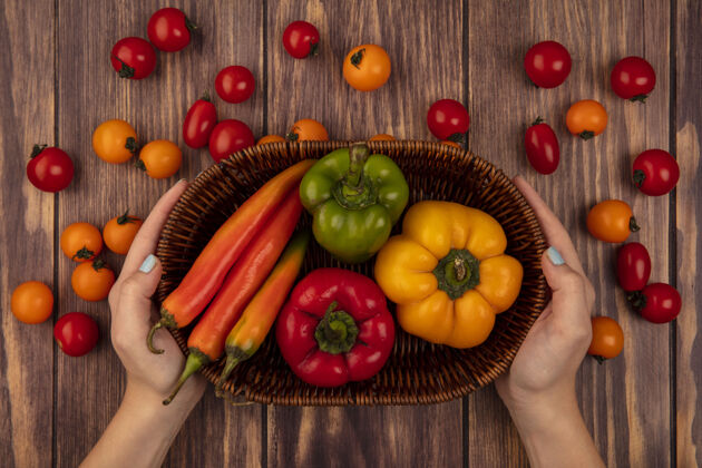 食物顶视图中的女性手拿着一桶新鲜的辣椒和樱桃番茄隔离在木墙上有机番茄手工