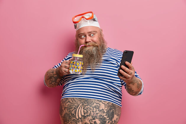 穿着积极的胖子喝淡水 通过手机拍照 戴着游泳浮潜面罩 穿着小号水手衬衫腹部护目镜超重