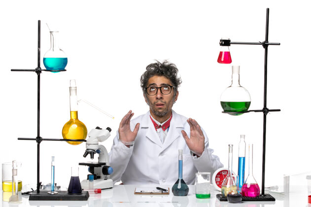 人前视图穿着白色医疗服的男科学家坐在桌子前 带着解决方案坐化学人