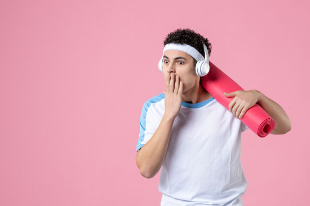 视图正面图：穿着运动服的年轻男性 粉色墙上有瑜伽垫和耳机垫子人水平