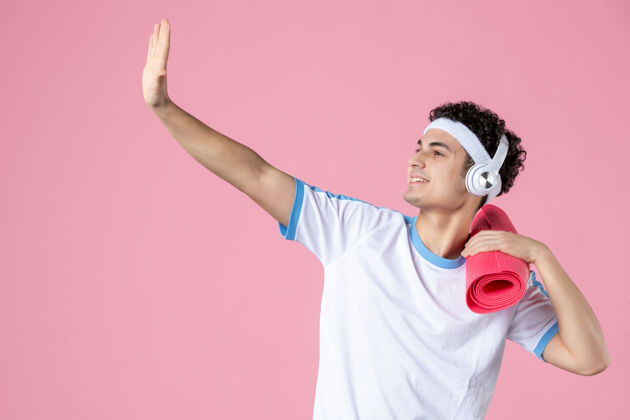微笑正面图穿着运动服的年轻男性 粉色墙上有瑜伽垫运动健身房人物