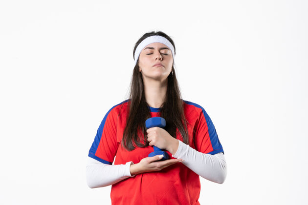 前面正面图穿着运动服的年轻女性在白墙上用哑铃锻炼运动人运动