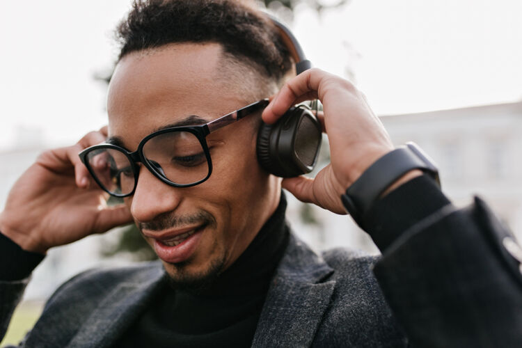 肖像可爱黑人的特写照片 留着时髦的发型 闭着眼睛听音乐戴着眼镜的疲惫的非洲男人戴着耳机欣赏歌曲的照片年轻男孩男人