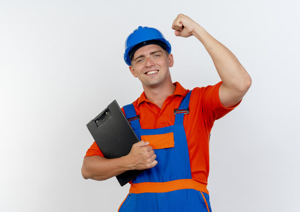 男性面带微笑的年轻男性建筑工人身穿制服 头戴安全帽 手持写字板 向白色举起拳头制服拳头举起