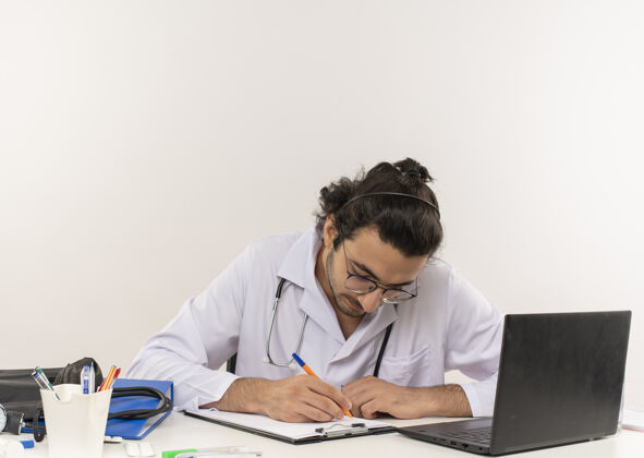 医疗年轻的男医生戴着医用眼镜 穿着医用长袍 坐着听诊器手势医生办公桌