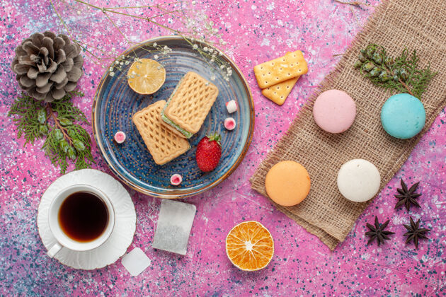 粉俯瞰美味的华夫饼 麦卡龙和粉红色表面上的一杯茶货币饼干生的