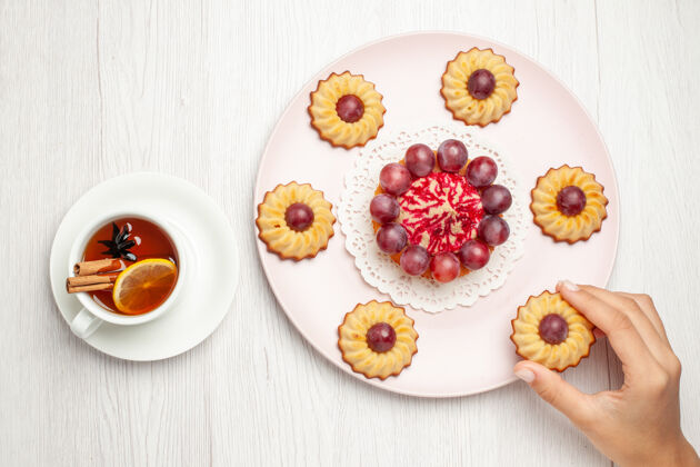 盘子俯瞰美味的葡萄蛋糕和一杯茶放在白色的桌子上甜点饼干派饼干美食午餐茶