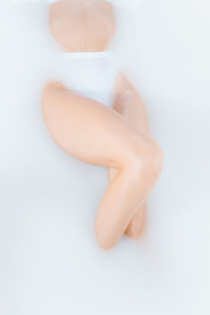 人腿部和腹部在牛奶浴中用柔和的白光封闭女性身体光Spa辉光