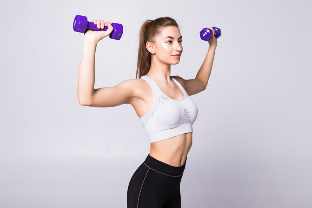 哑铃健康的女人 带着哑铃在白墙上锻炼健身馆的概念欢呼运动强壮