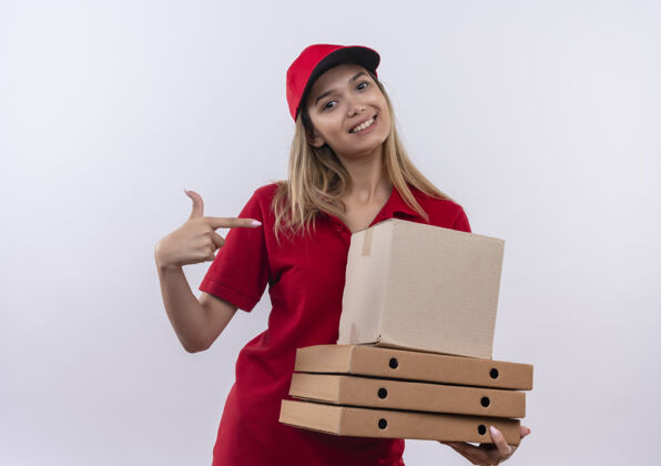 交货面带微笑的年轻送货女孩身穿红色制服 戴着帽子 指着许多白色的箱子手势女人年轻