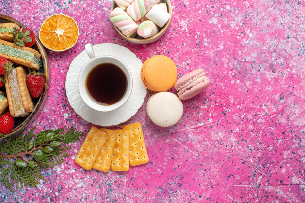 茶俯瞰美味的华夫饼干与法国马卡龙和一杯茶在粉红色的表面麦卡龙咖啡糖果
