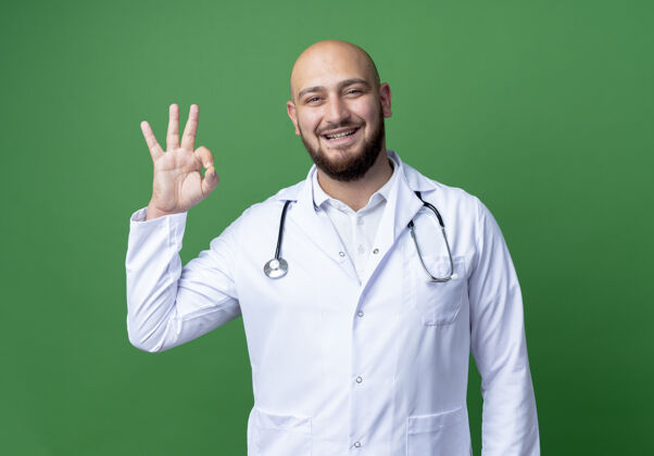 绿色微笑着的年轻男医生穿着医用长袍和听诊器 在绿色上显示出良好的姿势医生微笑听诊器