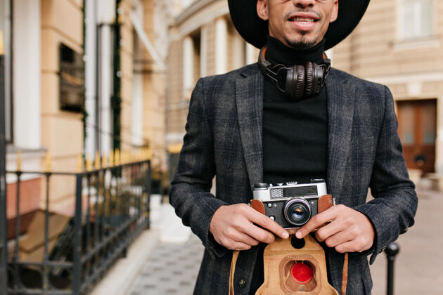 街道有灵感的非洲男人穿着黑色衬衫站在街上 手里拿着相机穿着考究的摄影师的户外镜头男人高兴积极