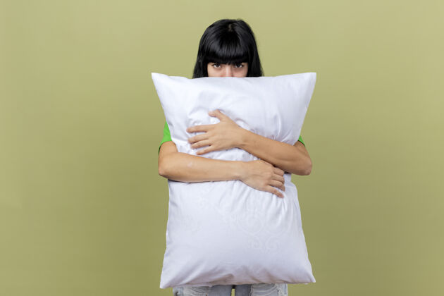 疾病年轻的生病的女人抱着枕头从后面看前面的枕头孤立在橄榄绿的墙上脸拥抱站立
