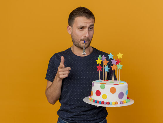 男人自信的帅哥拿着生日蛋糕吹着口哨 指着橙色墙上孤立的前方人蛋糕人