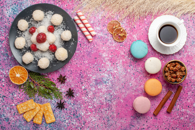 椰子俯瞰美味的椰子糖和法国马卡龙和浅粉色表面上的一杯茶饼干茶食物