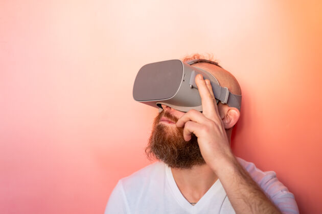 视频一个留着胡子的男人在工作室里戴着虚拟现实眼镜 背景是粉橙色的 这是一幅感人的肖像设备数码游戏