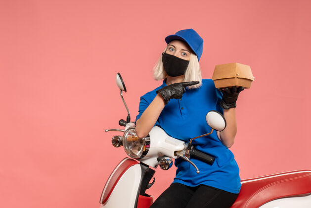 食品正面是戴着面具的女快递员 粉红色的小食品包装女信使服务摩托车