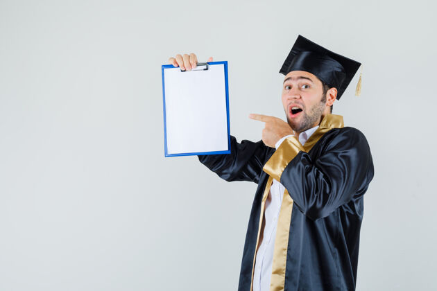 男人年轻人指着毕业制服的剪贴板 看起来很高兴前视图毕业聪明朋友